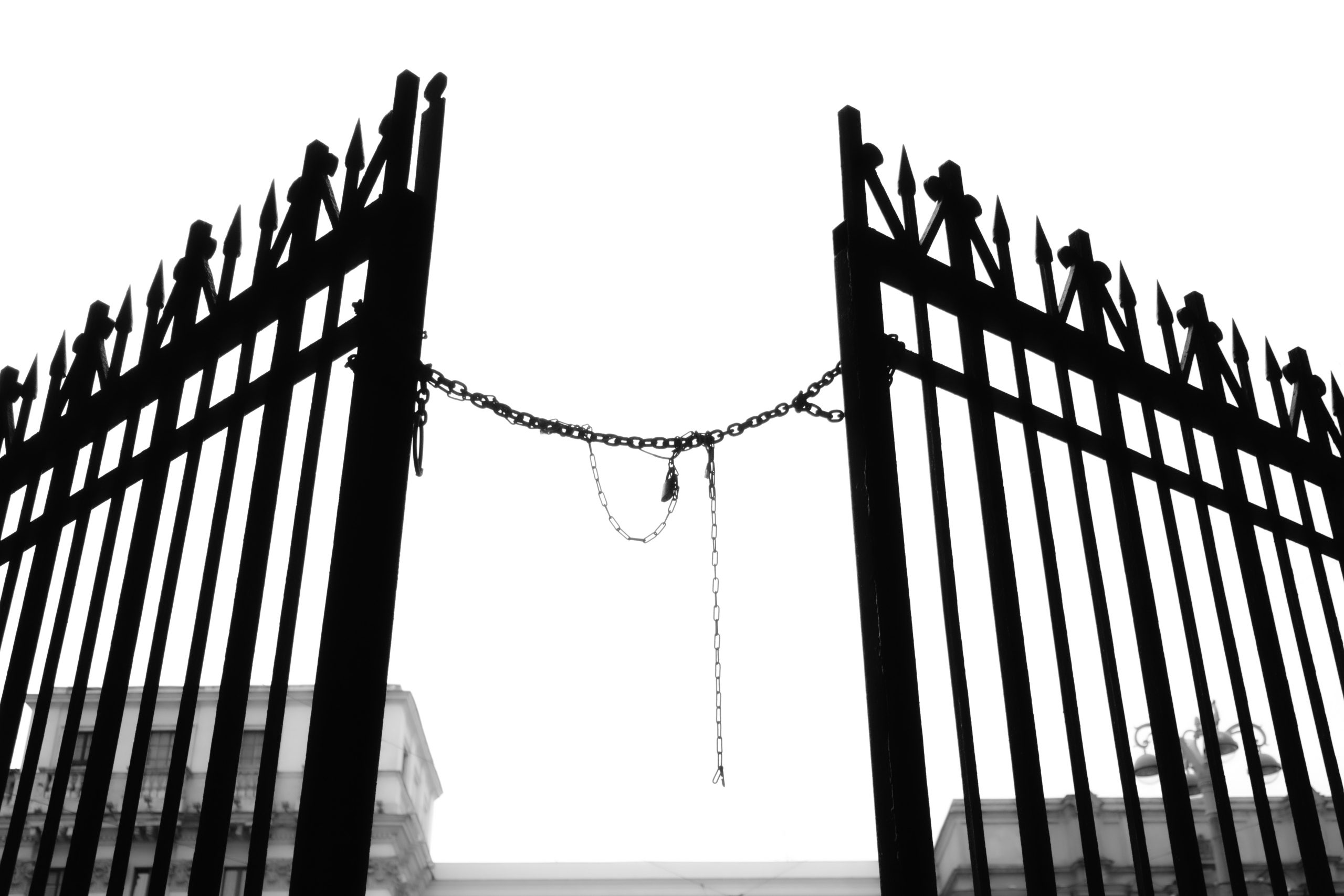 black and white photo of a fence that was chained shut but has been broken open. Breaking Barriers